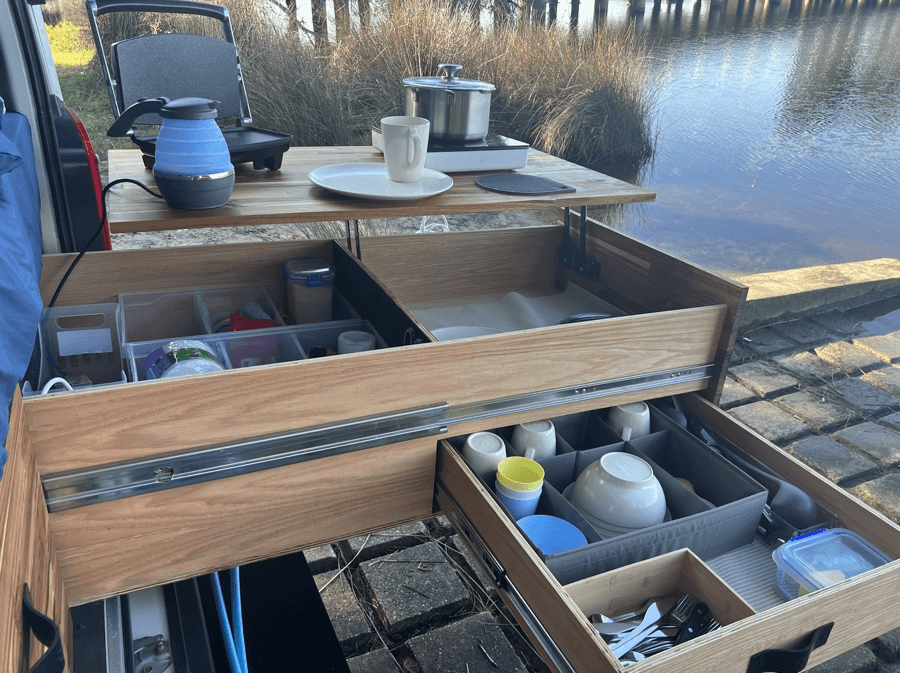 A camp kitchen drawer with cookware and utensils laid out at the rear of a campervan