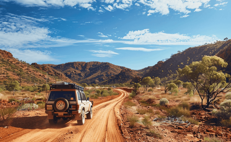 Red earth, sparse vegetation and dramatic rocky hills under a bright blue sky in Western Australia.