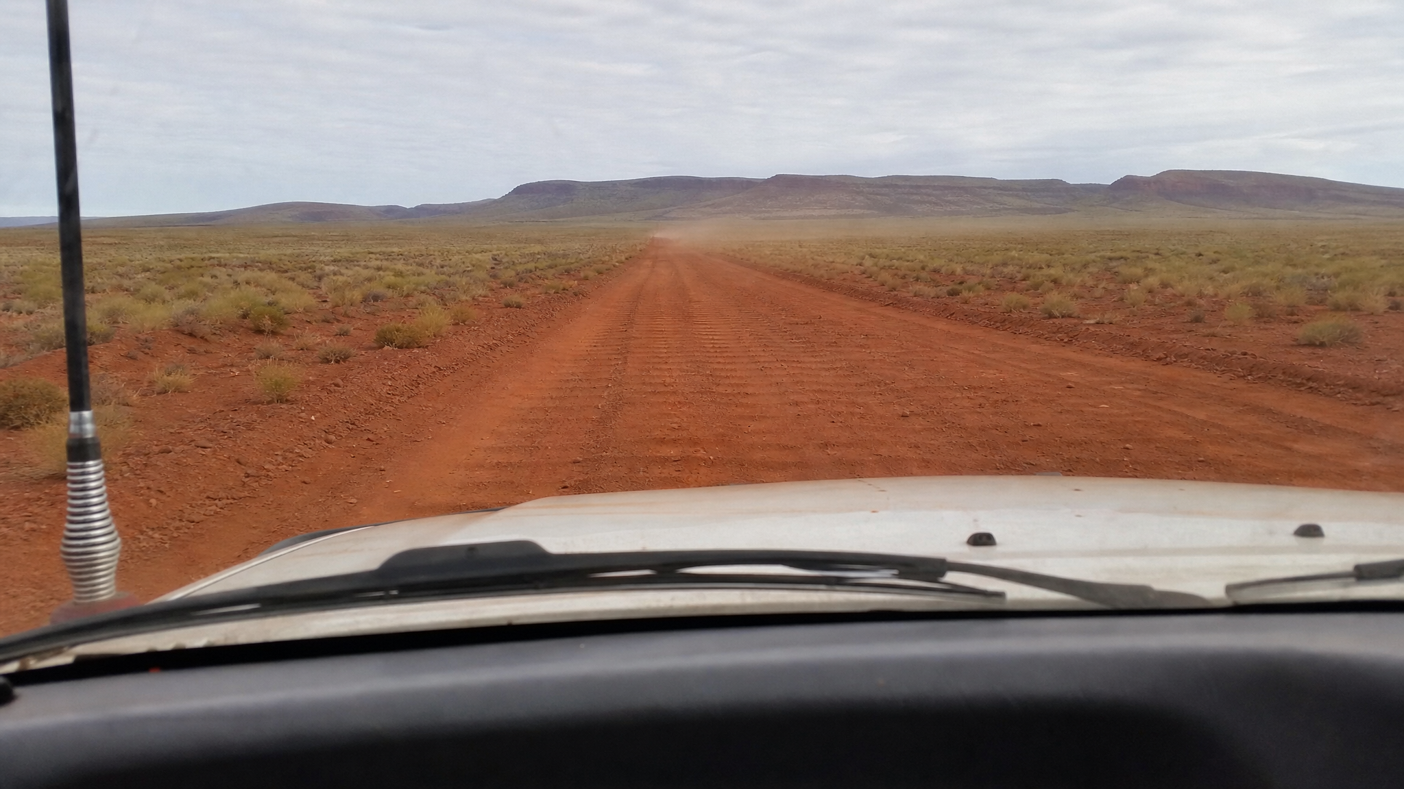 Driver's view through the windscreen of a corrugated red-dirt road in the Western Australia Pilbara